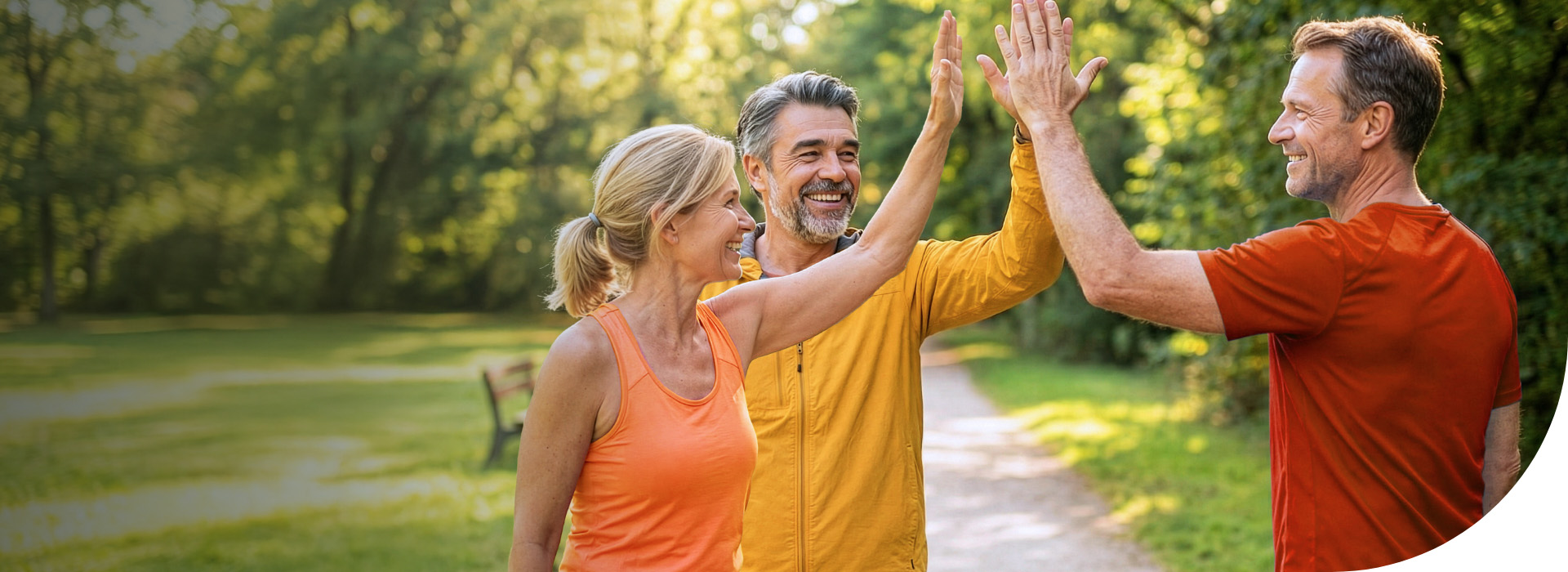 Drei Erwachsene im Park, die sich lächelnd abklatschen und gemeinsam aktiv sind